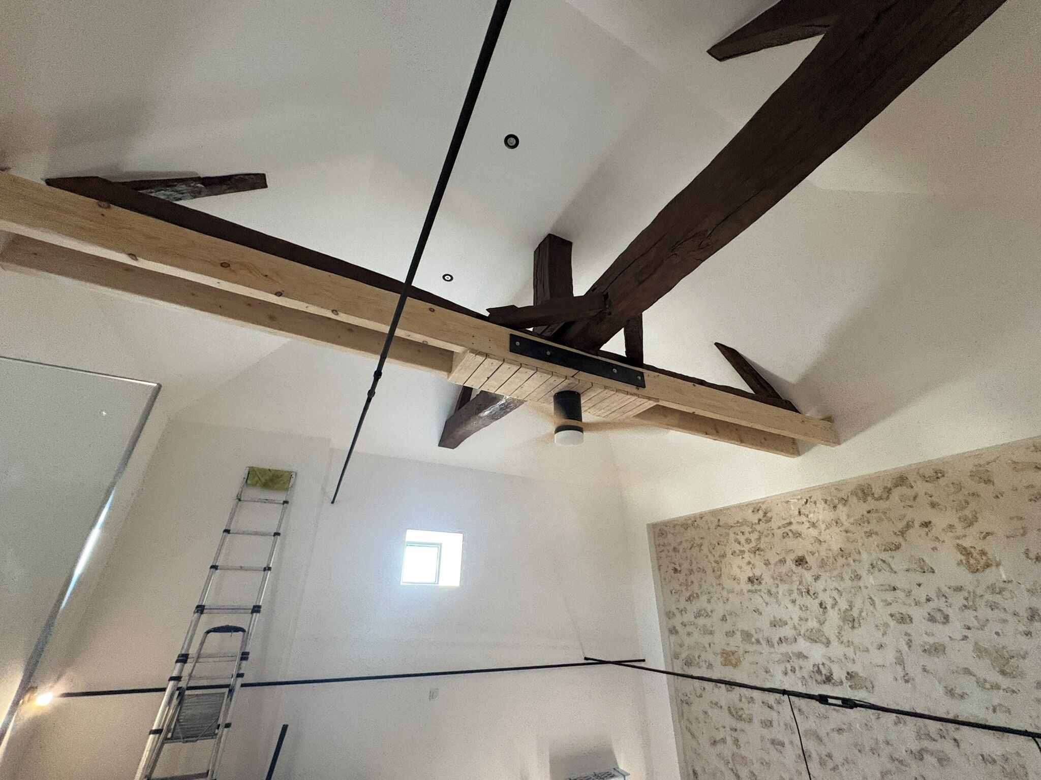 A room with exposed wooden beams, a ladder, and a window.