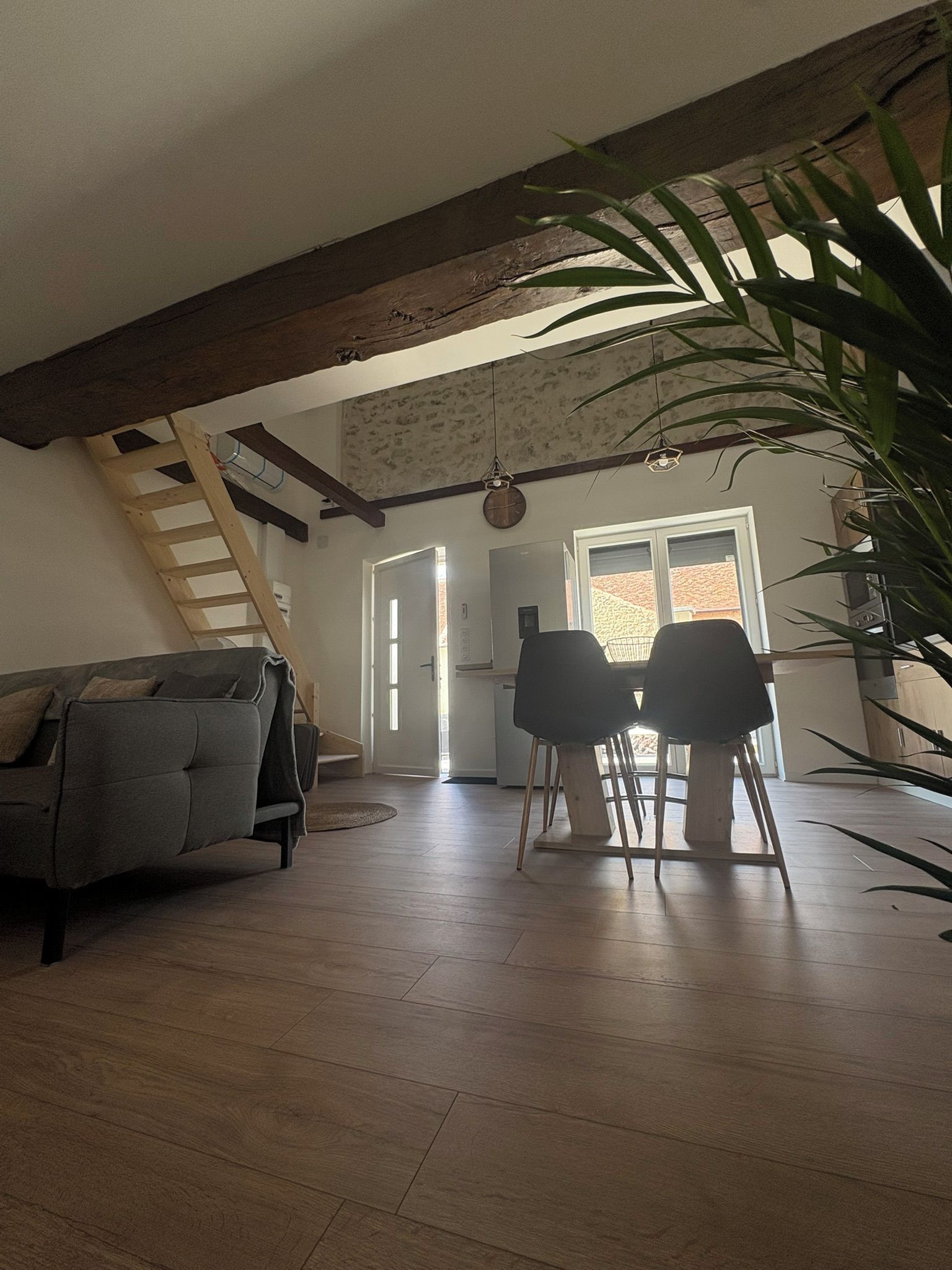 Una sala de estar acogedora con techo de madera, un sofá, dos sillones, una escalera y un ventanal grande.