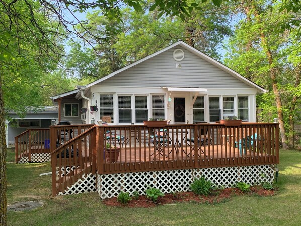 A single-story house with a covered porch, a fenced deck, and a sign that reads 'Sisters Cottage.'