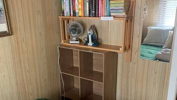 A room with a green bed, a wooden shelf with books, a fan, and a mirror reflecting a bed.