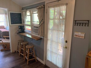 Una habitación acogedora con un banco de madera, una ventana con cortinas, un calentador en la pared y una pizarra con un mensaje de bienvenida.