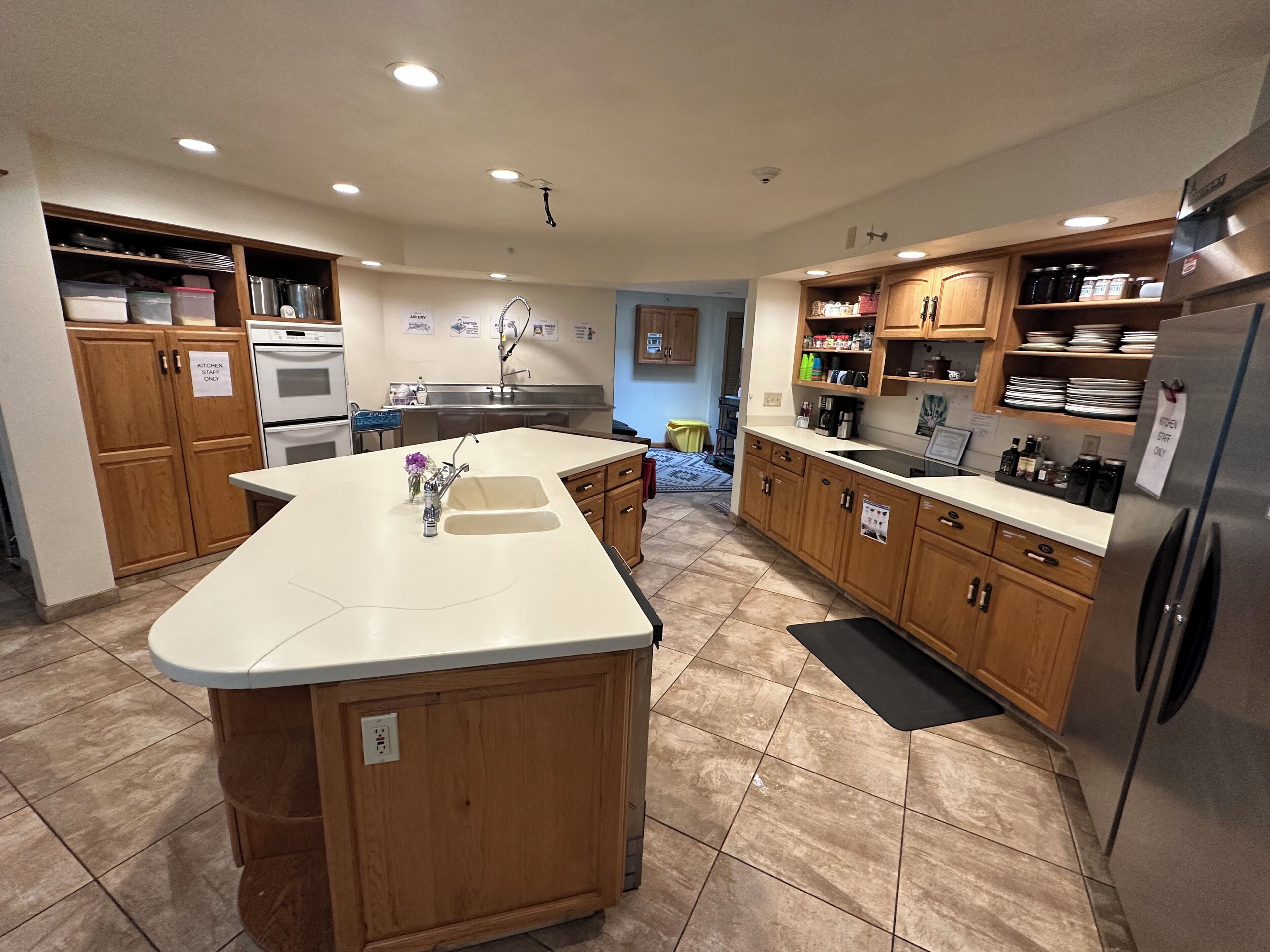 A modern kitchen with wooden cabinets, a central island, stainless steel appliances, and a tiled floor.