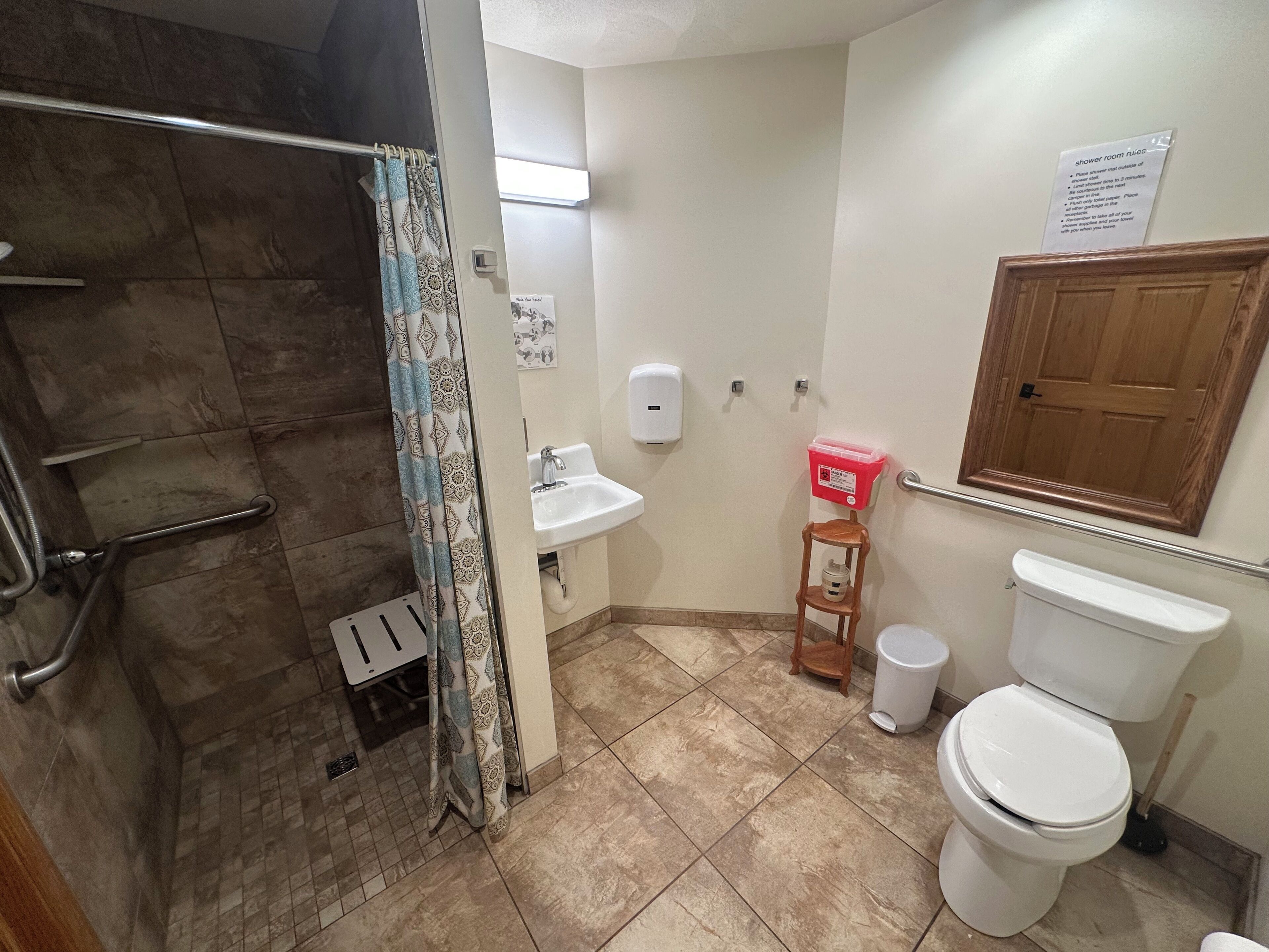 A bathroom with a shower, sink, toilet, and a wooden cabinet.