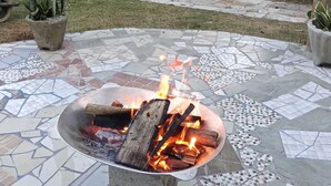 Un foyer extérieur avec des bûches qui brûlent, installé sur une terrasse carrelée.