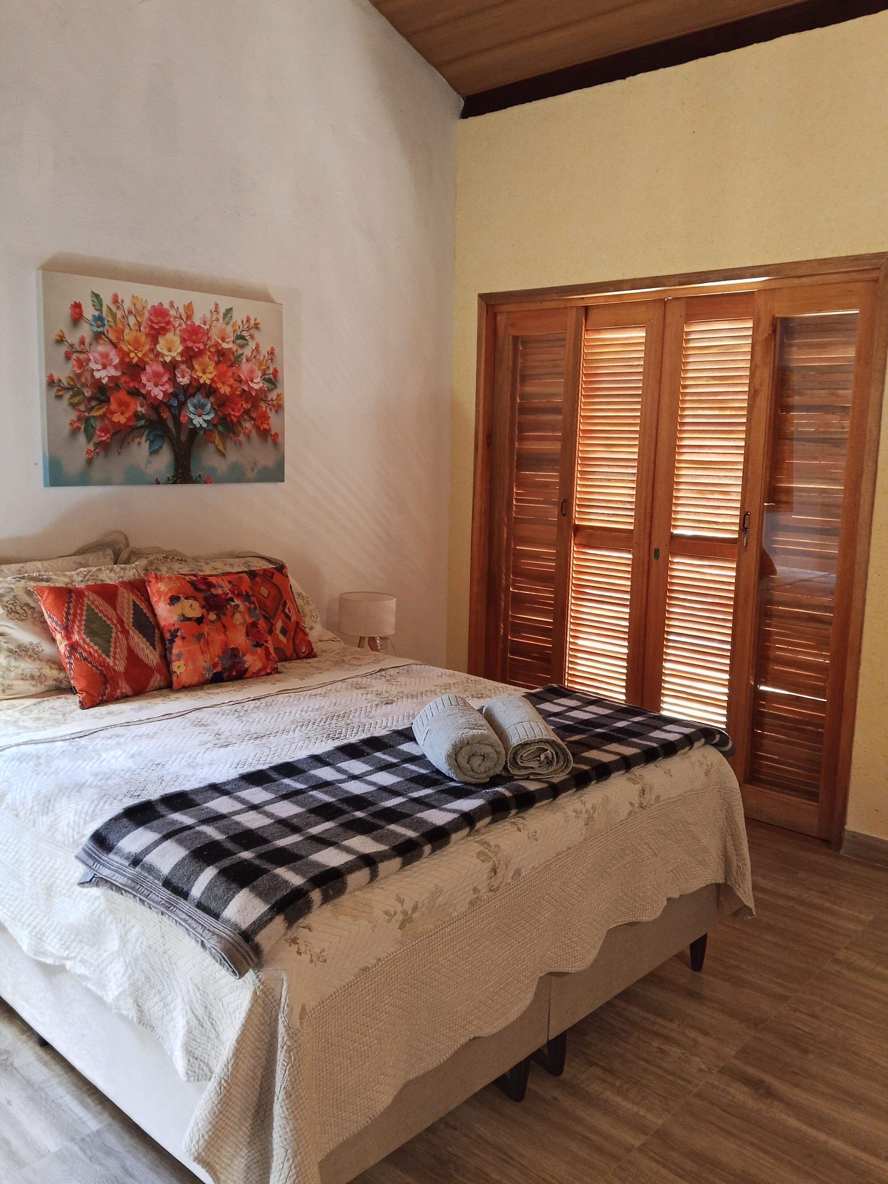 A bedroom with a bed, a painting, a wooden wardrobe, and a checkered blanket.