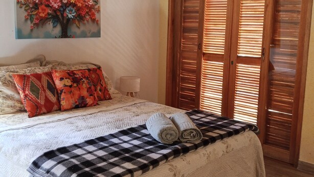 Une chambre à coucher avec un lit, un tableau, une armoire en bois et une couverture à carreaux.