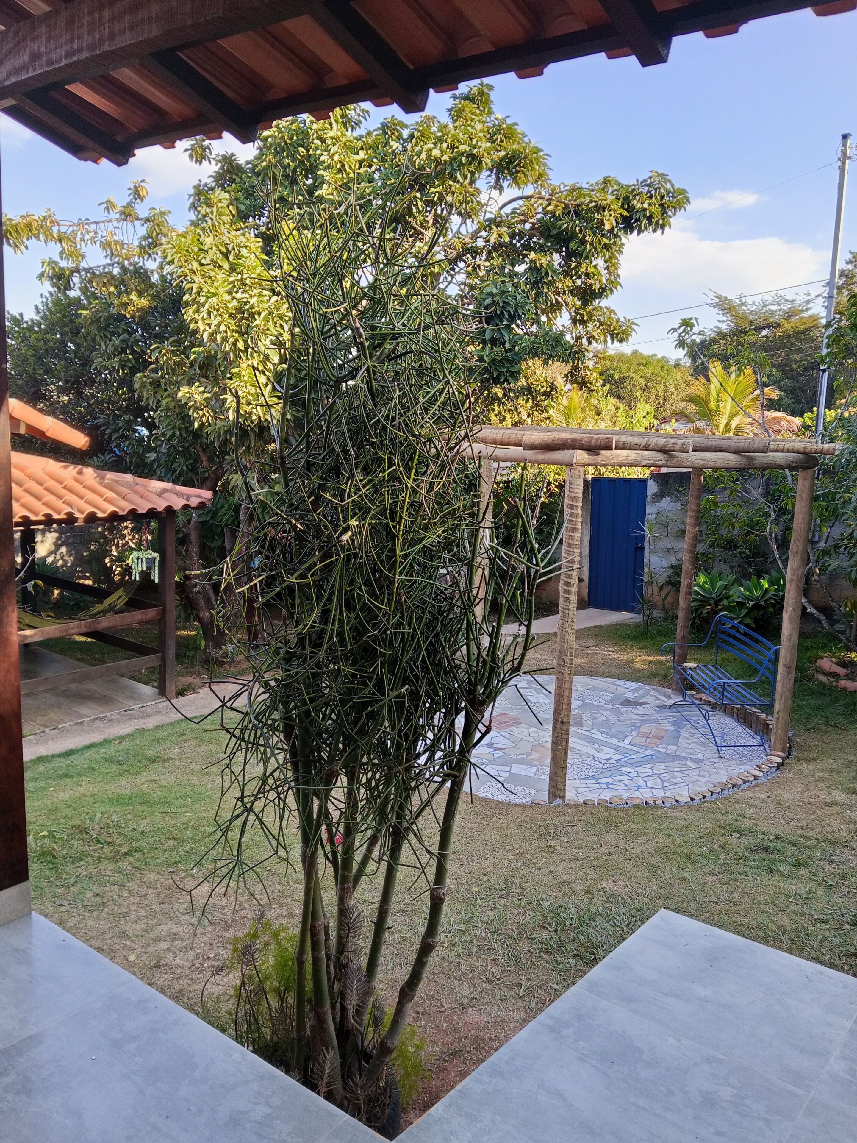A covered outdoor area with a tiled patio, a wooden pergola, and a blue gate.