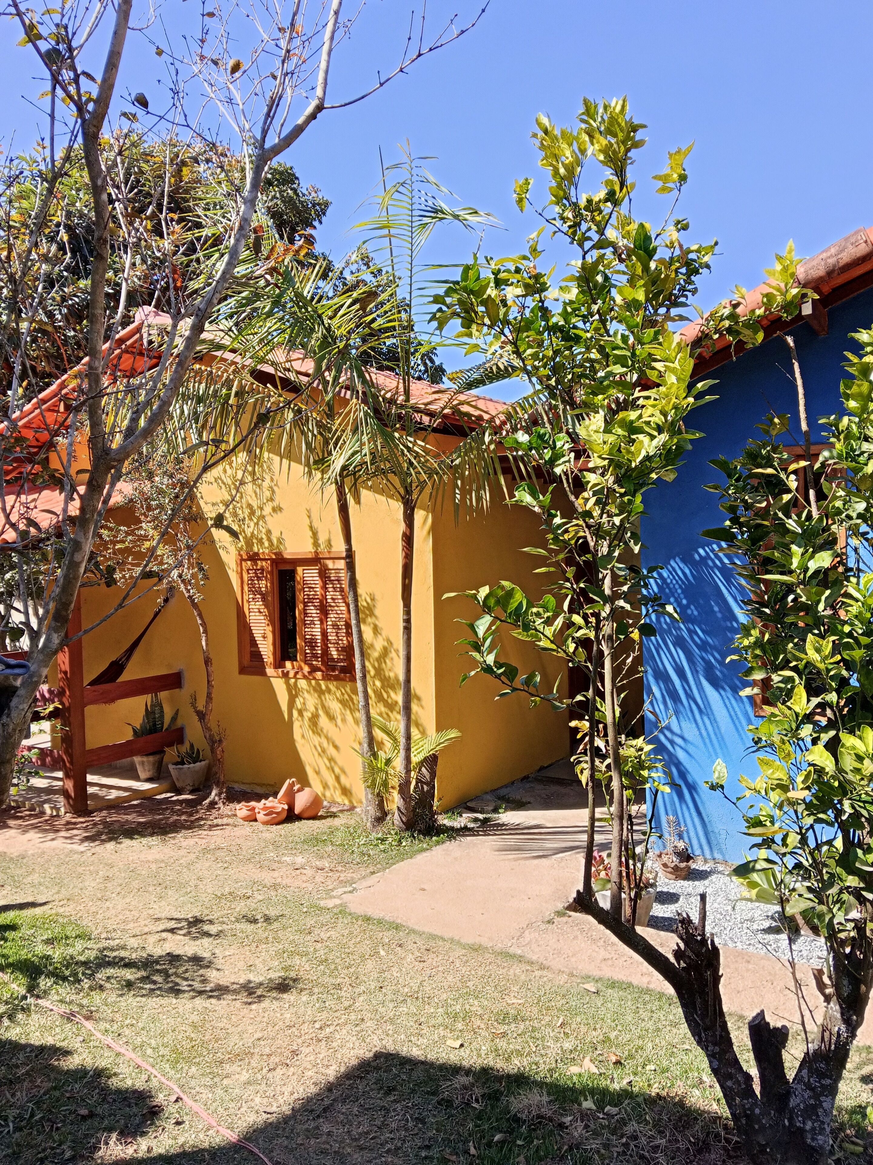 A yellow building with a red roof, surrounded by trees and potted plants.