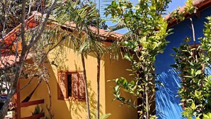 Un bâtiment jaune avec un toit rouge, entouré d’arbres et de plantes en pot.
