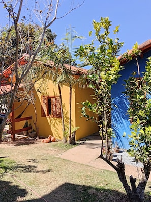 A yellow building with a red roof, surrounded by trees and potted plants.