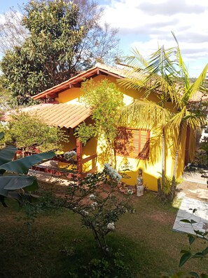 A yellow building with a tiled roof, surrounded by greenery and a palm tree.