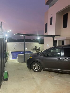 Un estacionamiento con un automóvil, una piscina y un edificio de techo plano.