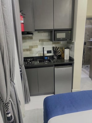 A compact kitchenette with a microwave, sink, and storage cabinets. - Deval Den (Enugu)
