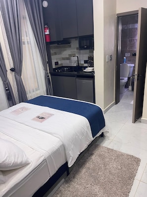 A bedroom with a bed, a small kitchenette, and a bathroom. - Deval Den (Enugu)