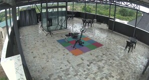 Un espacio al aire libre techado con suelo de baldosas, equipo de ejercicio y asientos.