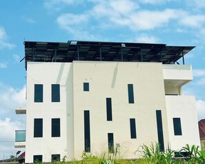 A multi-story building with a flat facade, several windows, and a rooftop with solar panels. - Deval Den (Enugu)