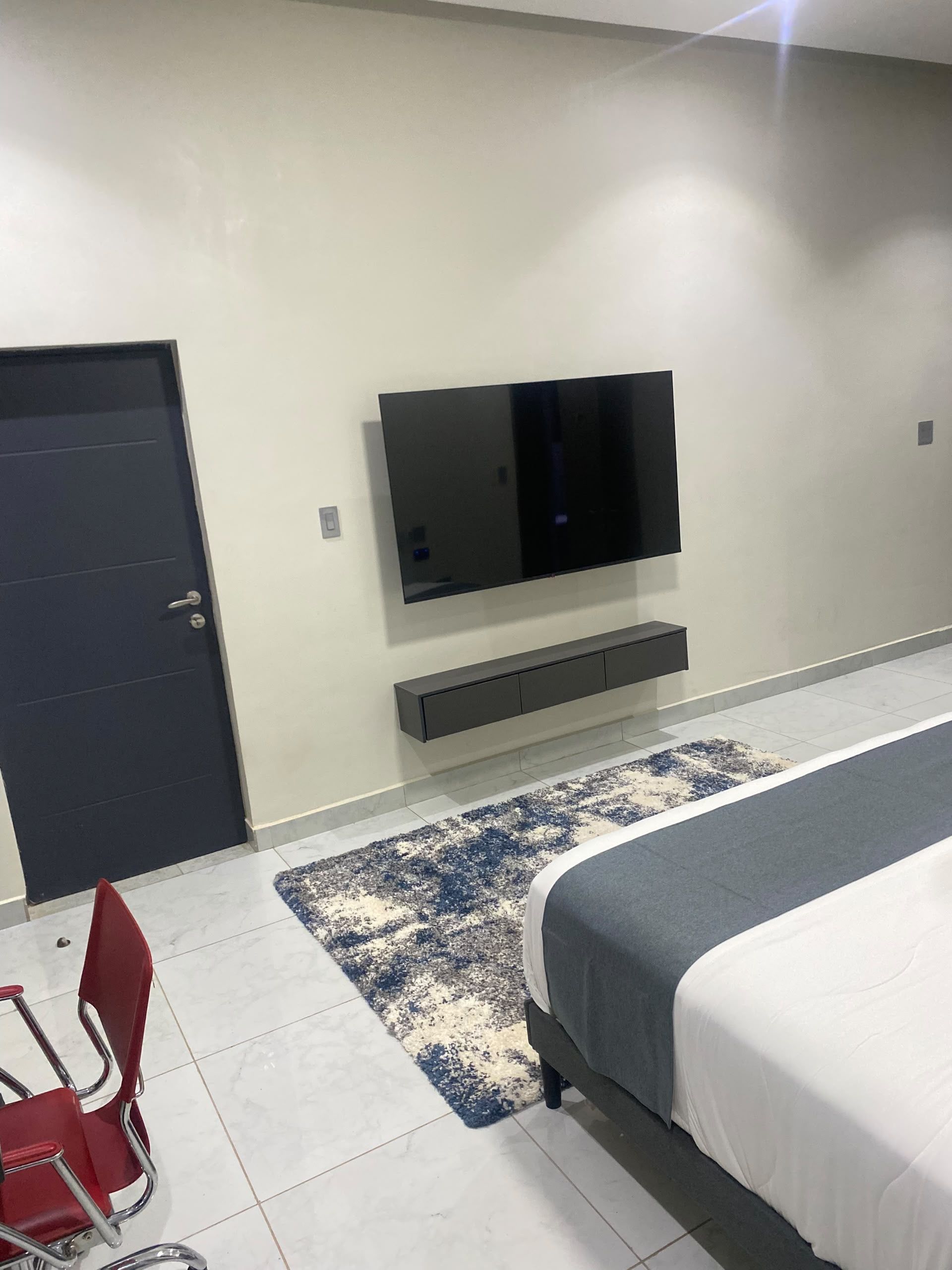 A bedroom with a bed, a TV mounted on the wall, a red chair, and a door.