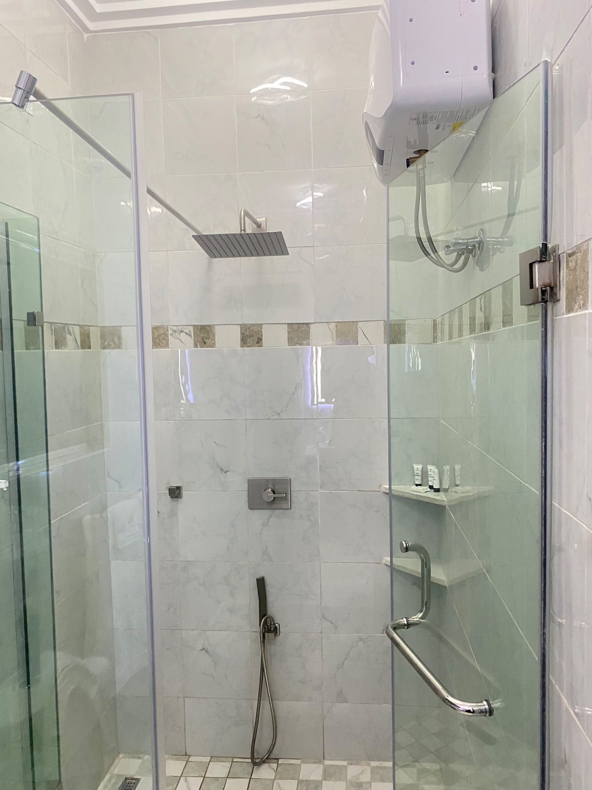 A glass-enclosed shower area with a handheld showerhead, a wall-mounted faucet, and a control panel.