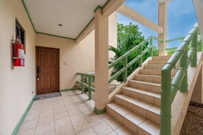 A hotel lobby with a wooden door, a fire extinguisher, a staircase with green railings, and a view of greenery outside. - Pacifico Azul Punta Plata 517 (Potrero)