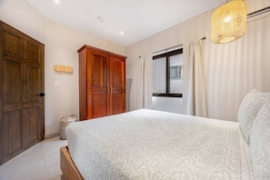 A bedroom with a large bed, wooden wardrobe, and a window with curtains. - Pacifico Azul Punta Plata 517 (Potrero)