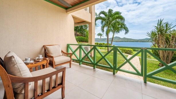 Un balcon donnant sur un lac, avec des meubles en bois et une rambarde verte.