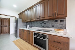 A modern kitchen with wooden cabinets, a stainless steel refrigerator, a built-in oven, and a stone backsplash. - Pacifico Azul Punta Plata 517 (Potrero)
