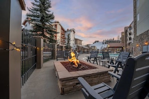 An outdoor seating area with a fire feature, surrounded by lounge chairs and a pool in the background. - Grand Lodge 259: Ski In/Ski Out 2BR, 2BA, Sleeps 6 - Pool, Hot Tub, Dogs OK (Crested Butte)