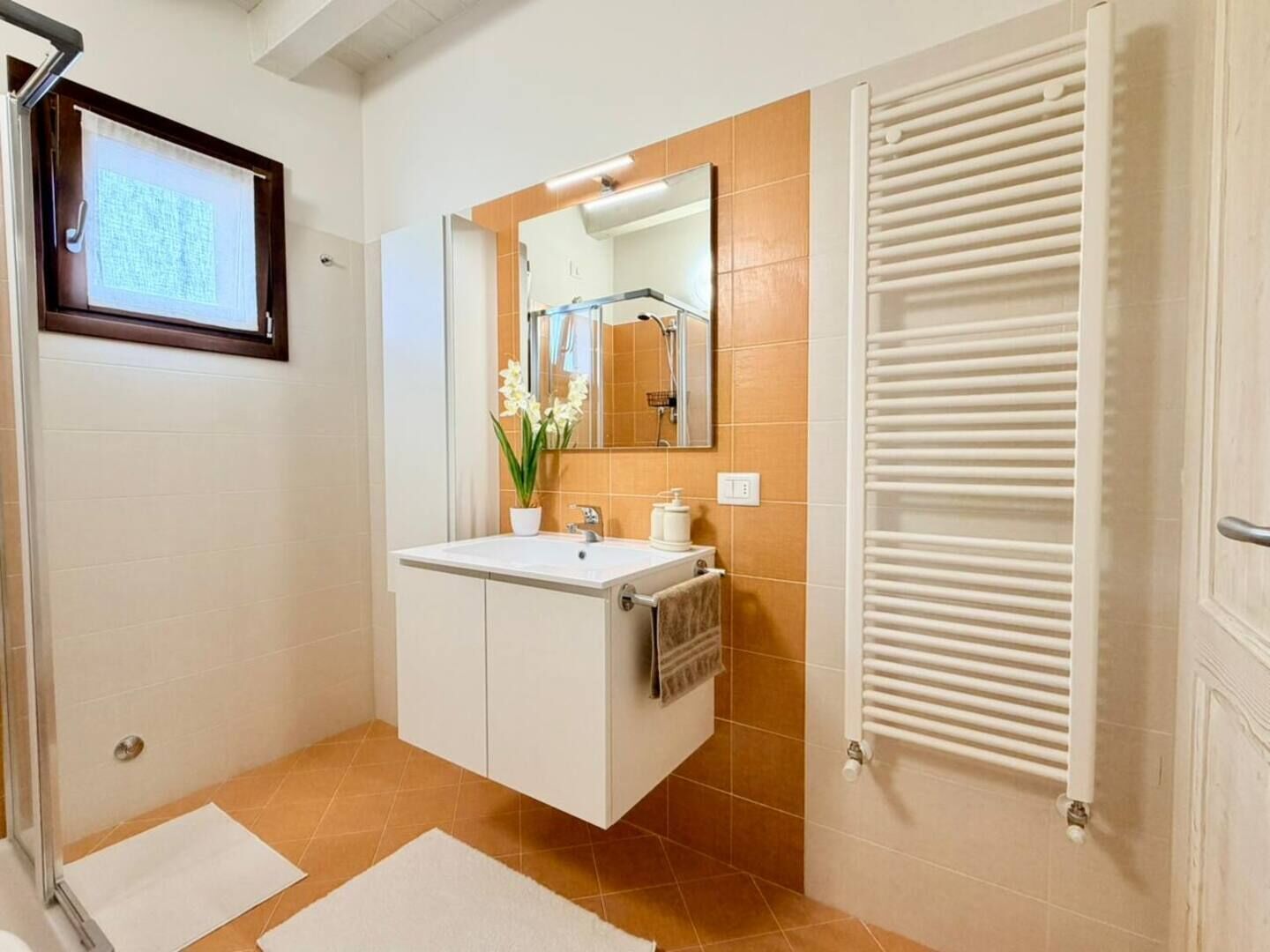 Un baño con lavamanos blanco, espejo, toallero y ducha.