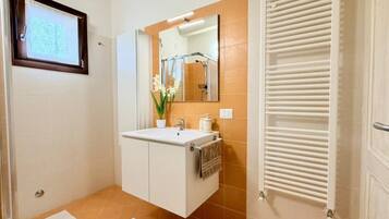 Un baño con lavamanos blanco, espejo, toallero y ducha.