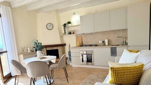 A modern kitchen with a built-in oven, a dining area with a table and chairs, and a living area with a sofa and a yellow pillow.