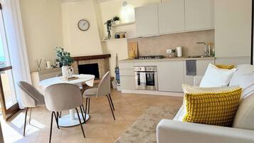 Eine moderne Küche mit integriertem Backofen, ein Essbereich mit Tisch und Stühlen und ein Wohnbereich mit Sofa und gelbem Kissen.