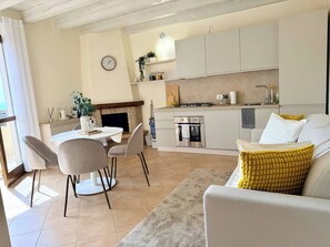 Una cocina moderna con horno empotrado, un comedor con mesa y sillas, y una sala de estar con sofá y almohadón amarillo.