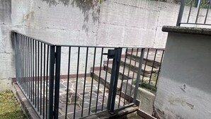A gated outdoor area with a stone-tiled floor and a concrete wall.