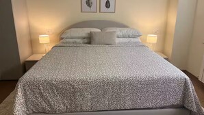A neatly made bed with a patterned bedspread, two wall-mounted framed leaf artworks, and bedside lamps on either side.