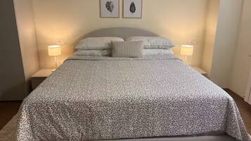 Un letto rifatto con cura, una coperta a motivi decorativi, due opere d'arte con foglie incorniciate a parete e lampade ai lati del letto.