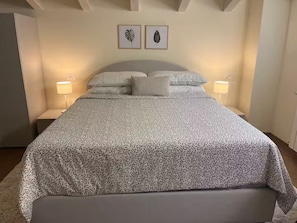 Una cama bien hecha con una colcha estampada, dos cuadros con motivos de hojas en la pared y lámparas de noche a cada lado.
