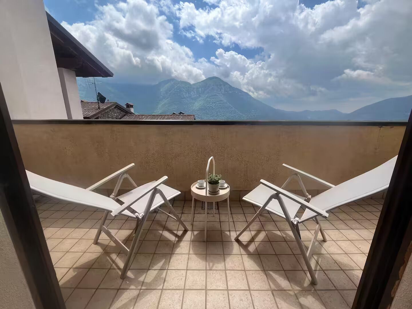 Un balcone con due poltrone bianche e un tavolino con una pianta e una tazza.