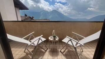 Un balcone con due poltrone bianche e un tavolino con una pianta e una tazza.