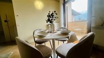 Un comedor con una mesa dispuesta para cuatro, sillas, un florero con flores y vistas al exterior.