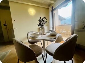 A dining area with a table set for four, chairs, a vase with flowers, and a view of the outdoors.