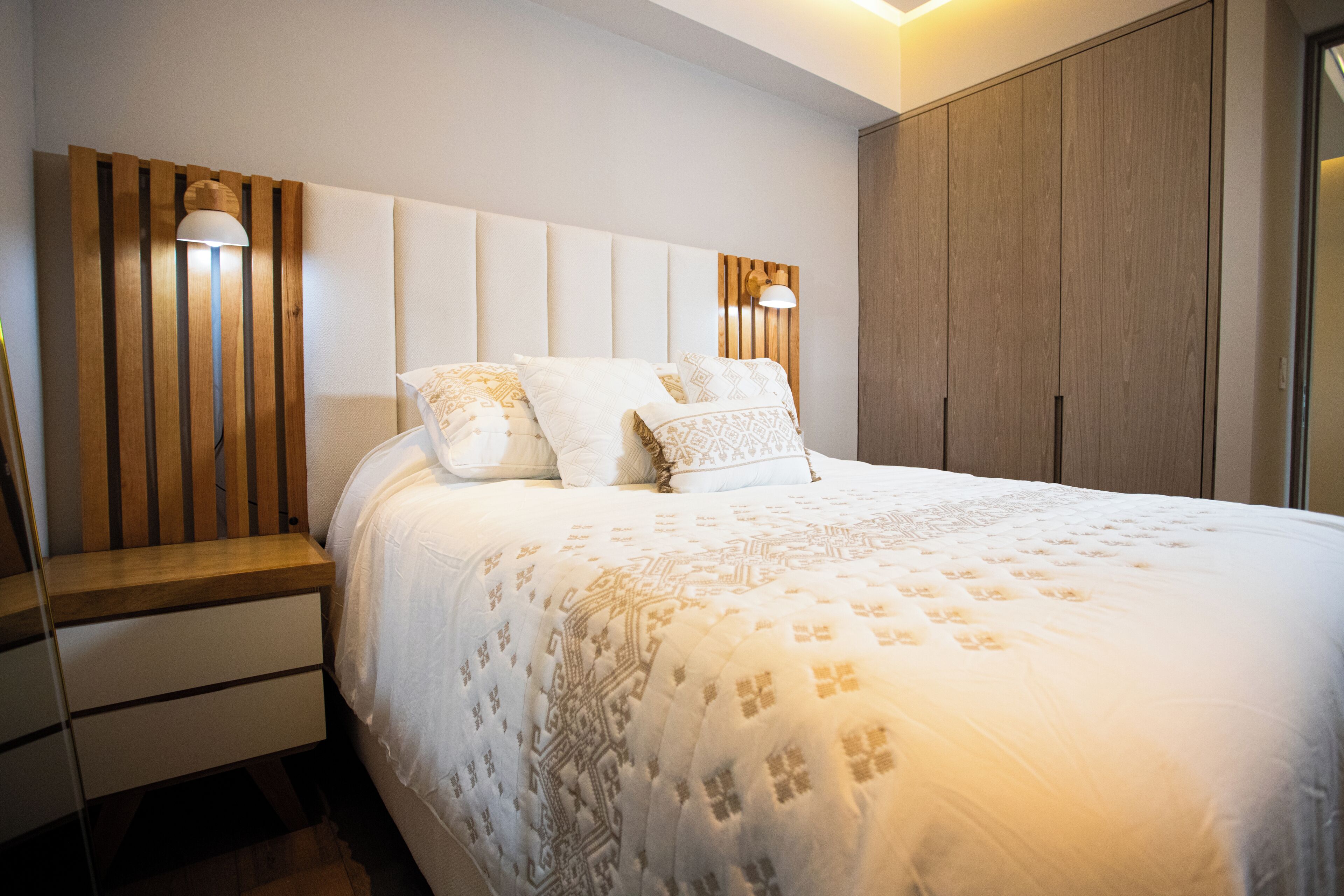Un dormitorio con una cama grande, una mesita de noche, un cabecero de madera y un armario.