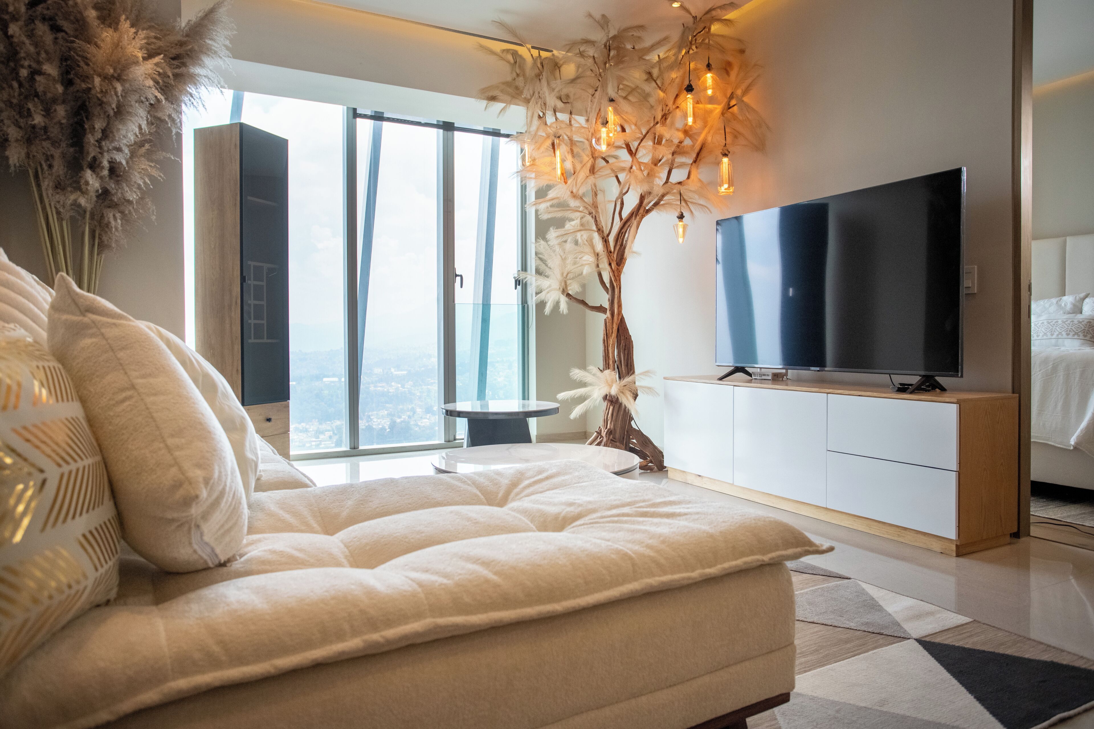 Une chambre moderne dotée d’un grand lit, d’un téléviseur à écran plat et offrant une vue sur la ville grâce à de grandes fenêtres.