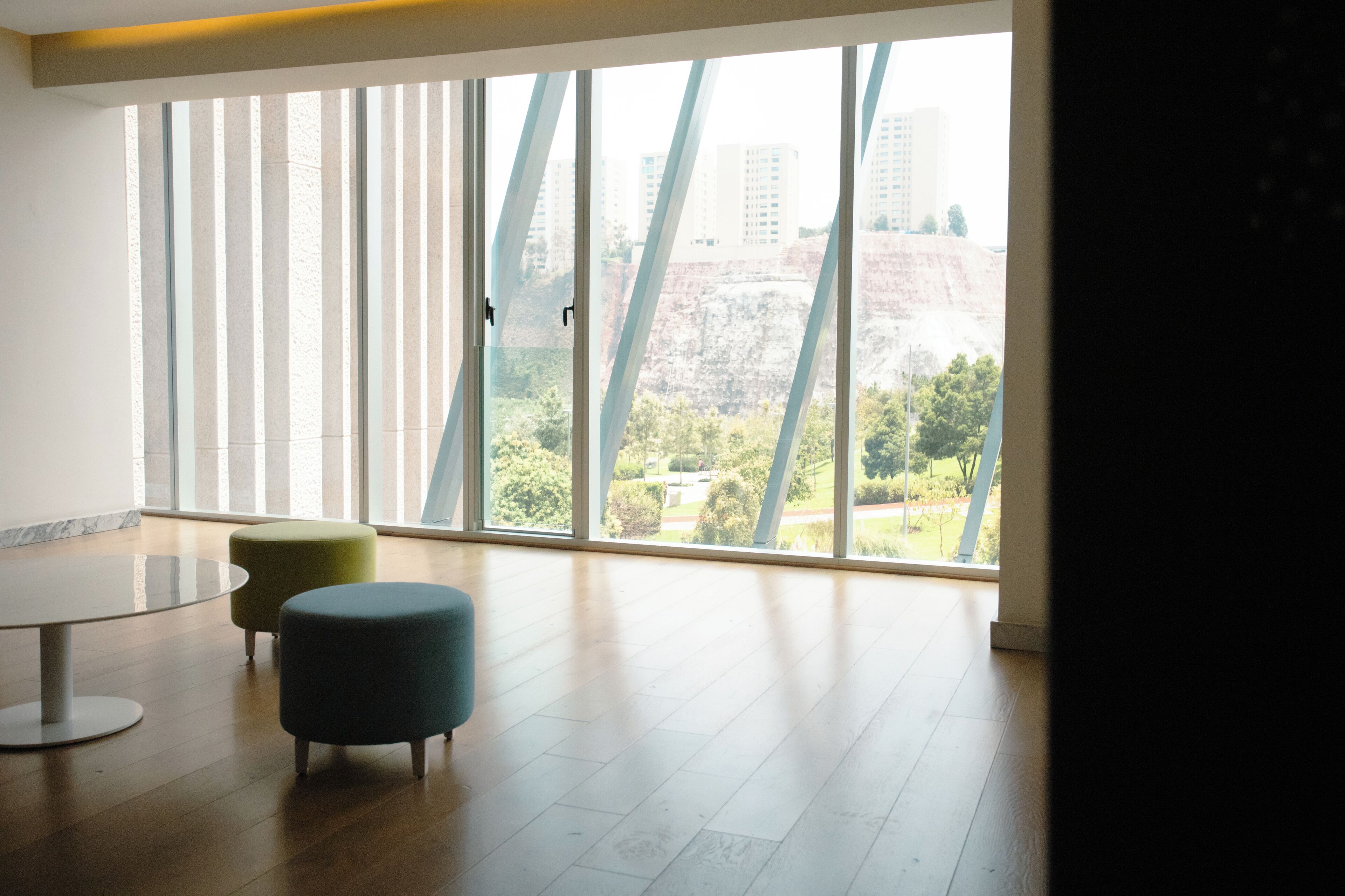 Una habitación amplia con un gran ventanal, una mesa redonda y dos otomanas.