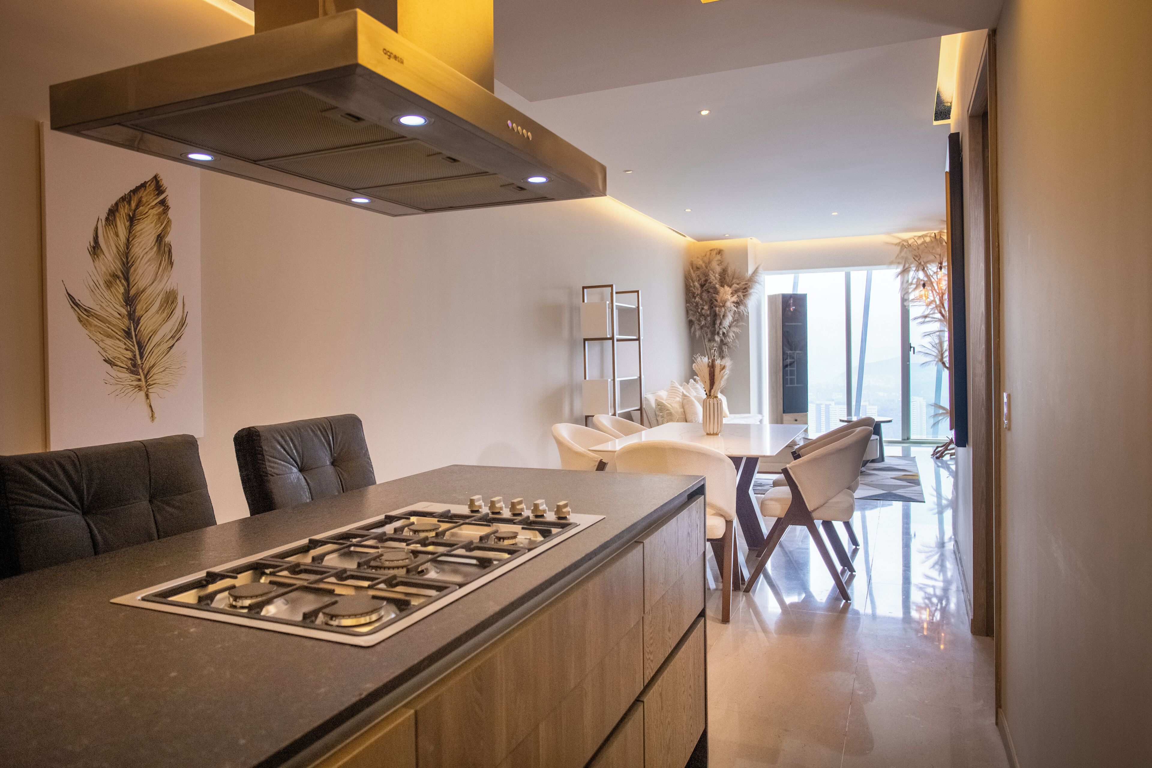 Cocina moderna con una isla central, comedor con una mesa y sillas blancas, y un amplio ventanal con vistas a la ciudad.
