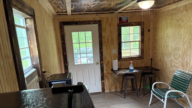 A room with a door, two windows, a table with a chair, and a bench.