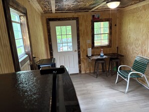 A room with a door, two windows, a table with a chair, and a bench.