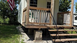 A small, single-story building with a porch, a flagpole with an American flag, and a wooden deck.