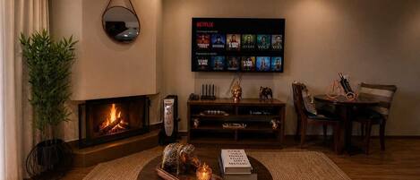 A cozy living room with a fireplace, a coffee table with decorative items, a bookshelf, and a wall-mounted TV displaying Netflix content.