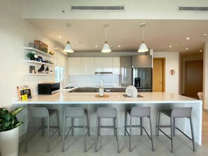 A modern kitchen with a central island, bar stools, pendant lighting, and built-in appliances.