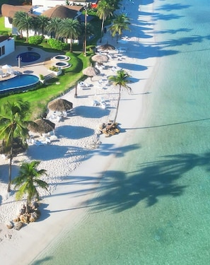A resort with a beach, palm trees, and a pool.